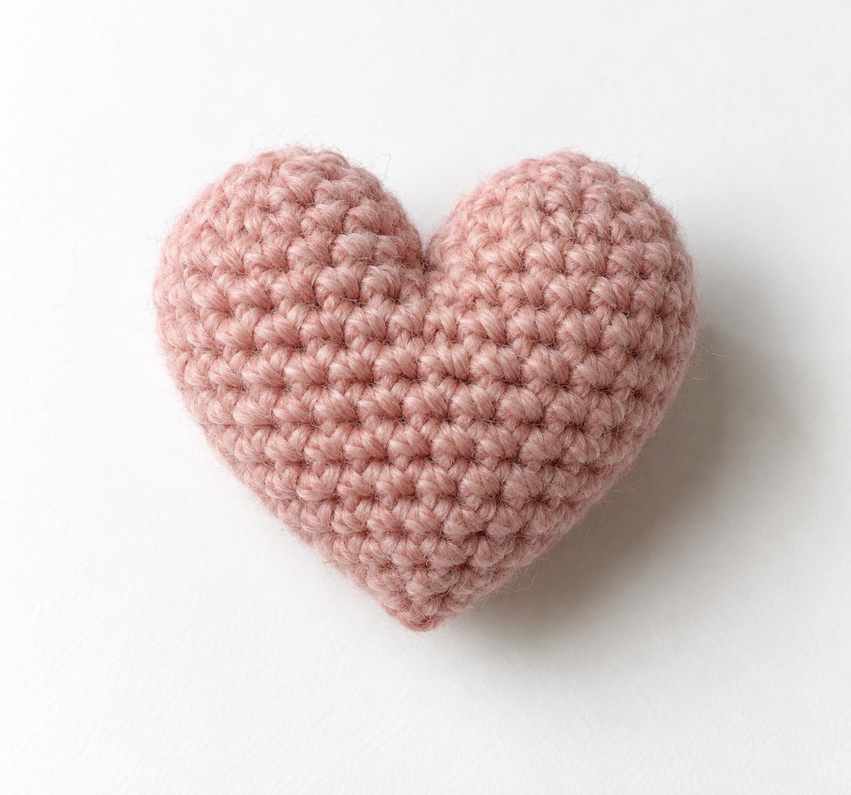 A pink crocheted heart with two rounded lobes and a pointed tip, worked in single crochet