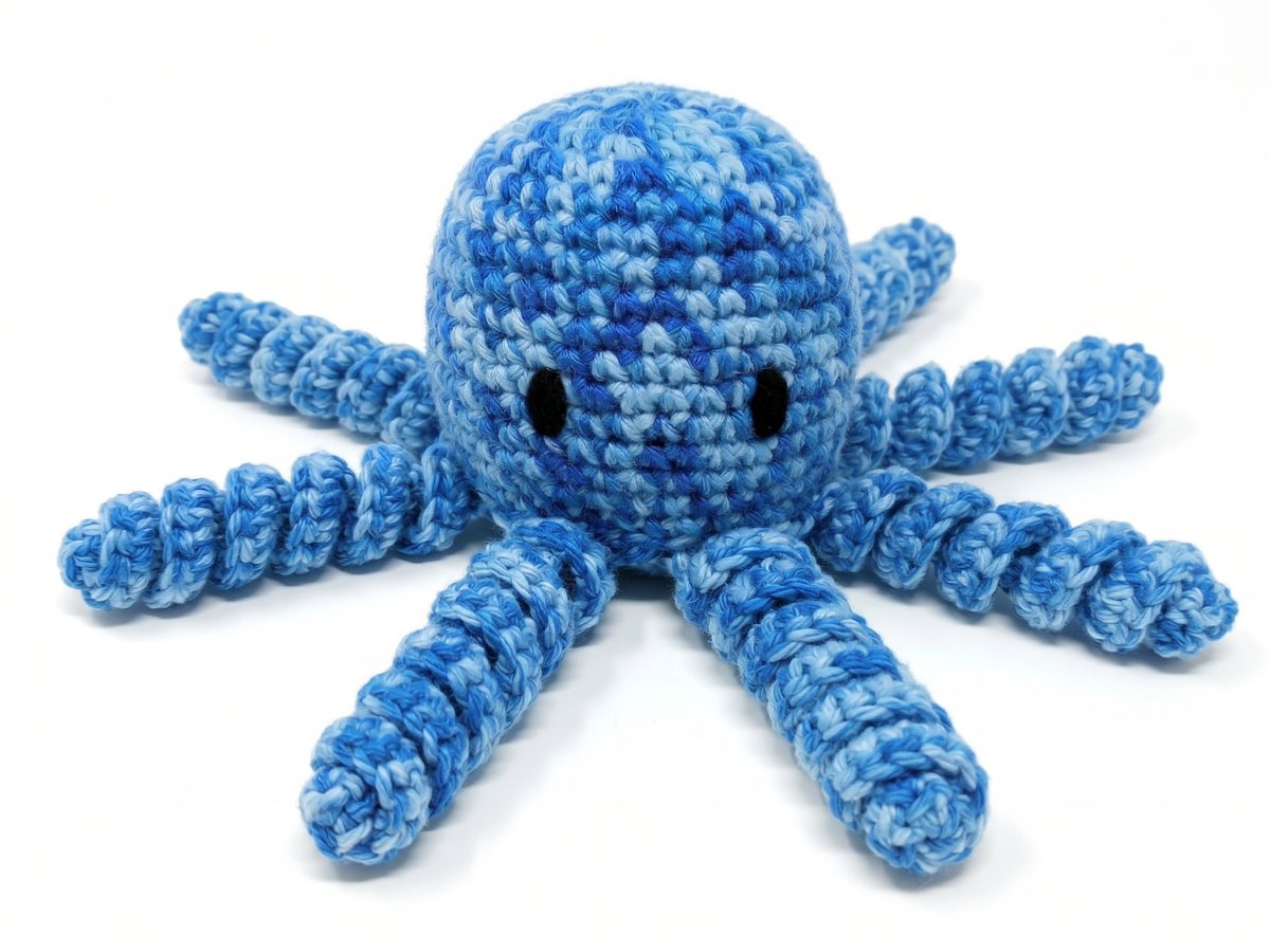 A crocheted amigurumi octopus in variegated blue yarn, with a round body, black eyes and curly corkscrew legs